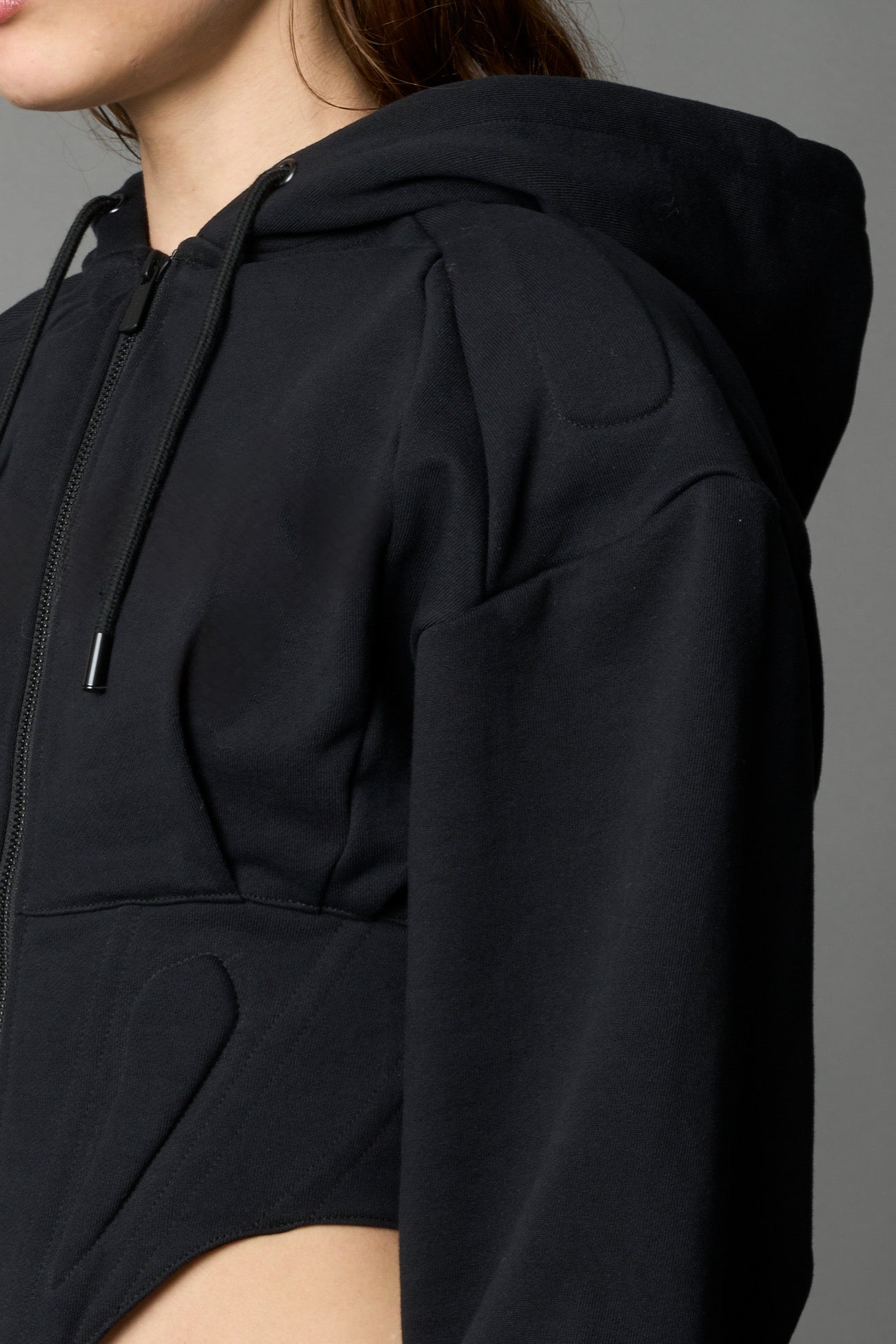 model in a black cropped hoodie featuring structured corset-style paneling embroidered across the chest in tonal black
