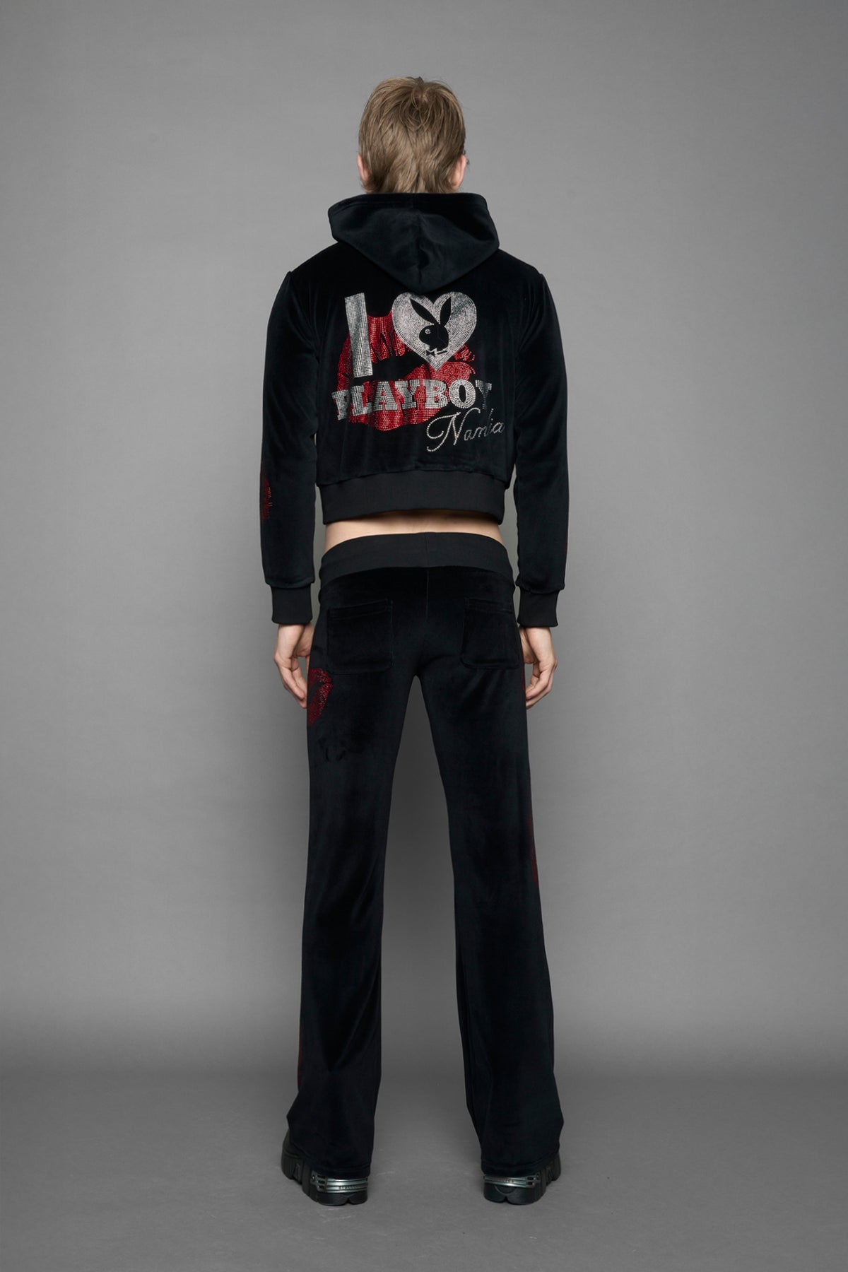 A female model wearing a black velvet zip-up hoodie with red sequined lip-print patches on the chest and sleeve, featuring white 'Namilia' embroidery on the left chest, photographed against a solid gray studio background.