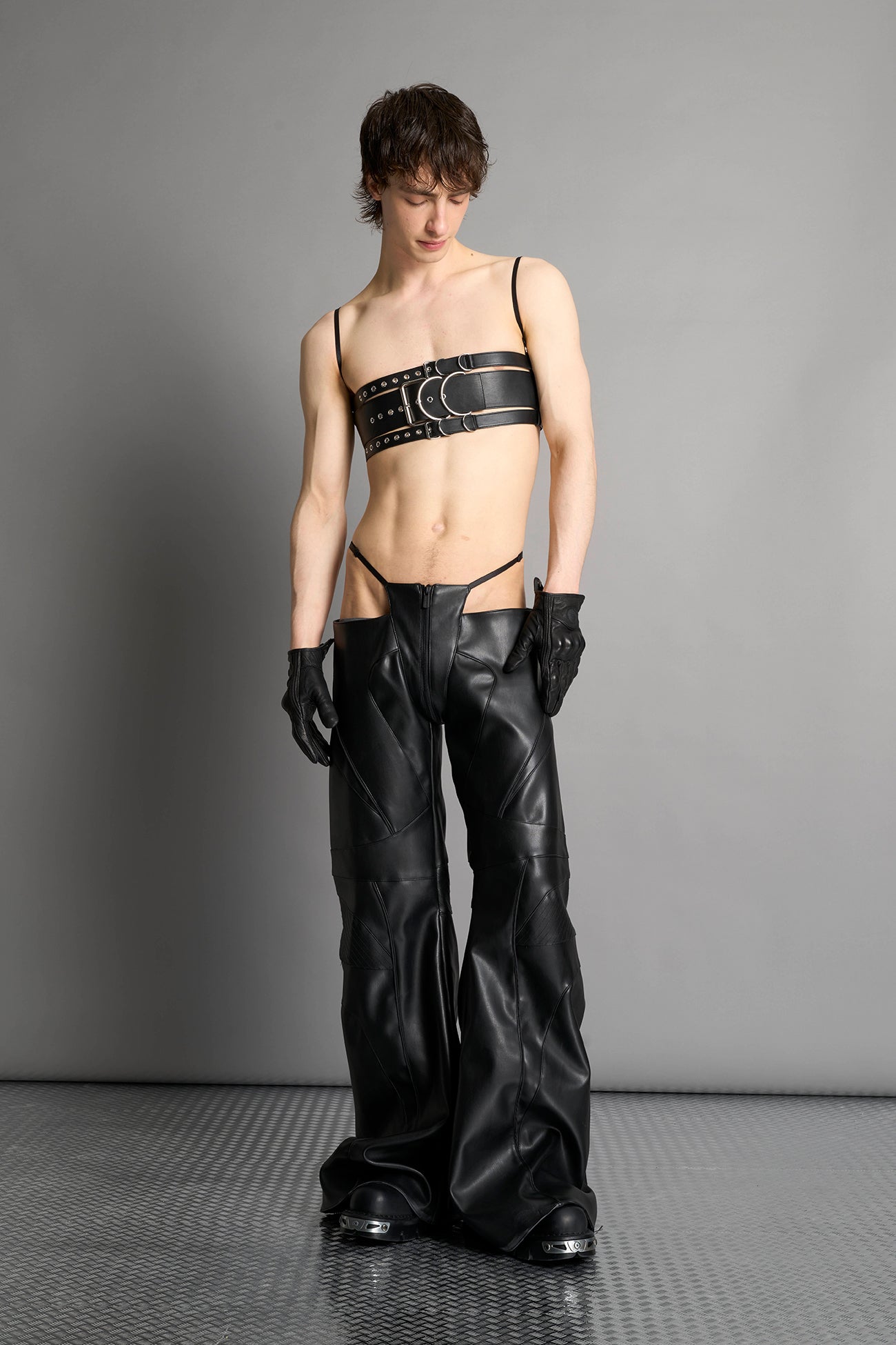 Black vegan leather belt top with three adjustable grommet straps, oversized metal buckles, and circular hardware – edgy bondage-inspired crop top for festival or clubwear.
