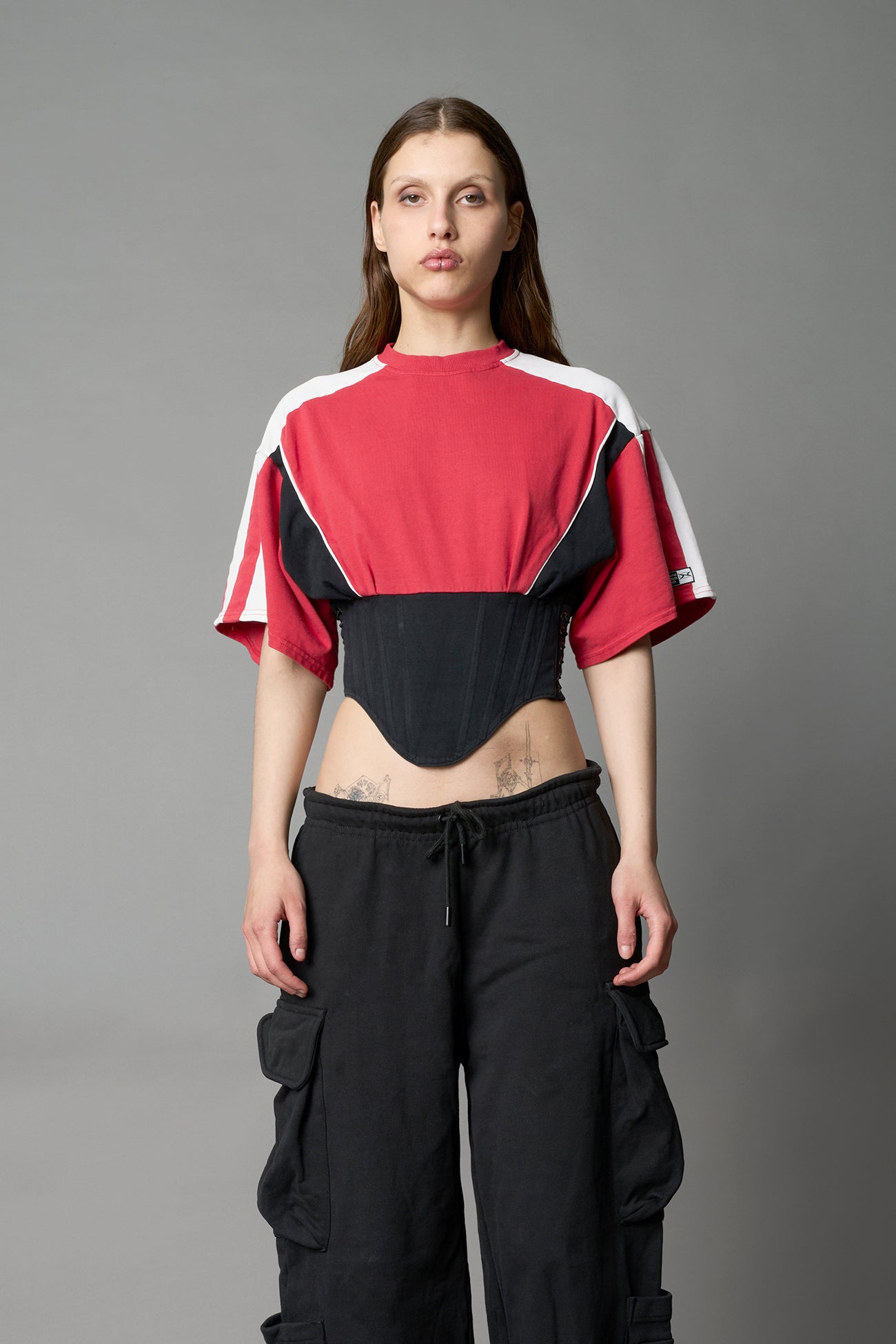 Front view of model in red Namilia Corset-T shirt with sculpted corset-style waist, curved hemline, and oversized sleeves,
