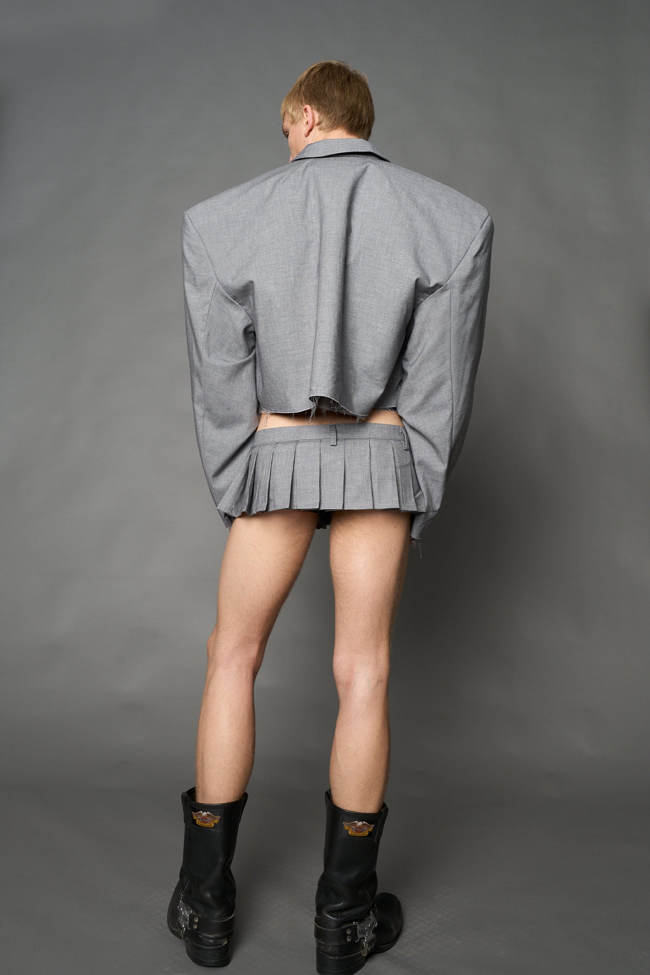 Grey ultra-mini pleated skirt with low-rise waist, belt loops, raw hem detailing and deconstructed tailoring by Namilia.