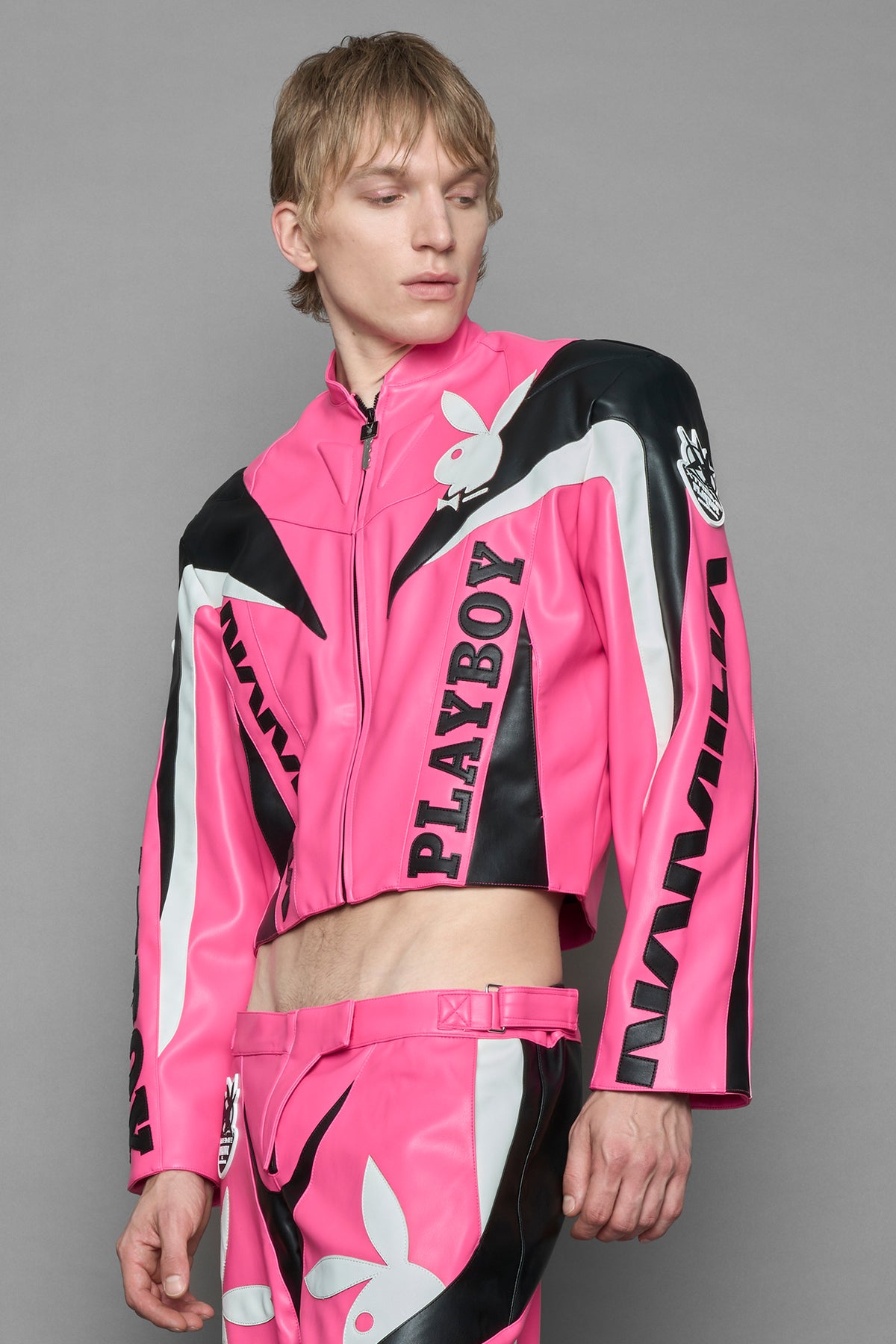 model wearing pink vegan leather zip-up jacket with black PU leather 'Namilia' and 'Playboy' embroidery and black and white paneling. On the left chest there is a white Playboy Bunny Embroidery.
