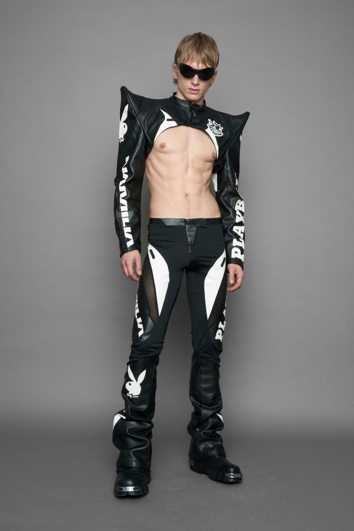 model wearing a black and white form fitted Pants with PU Leather Embroidery of 'Namilia', 'Playboy'. The pants have black Mesh fabric panels and are slightly flared from knee to hem