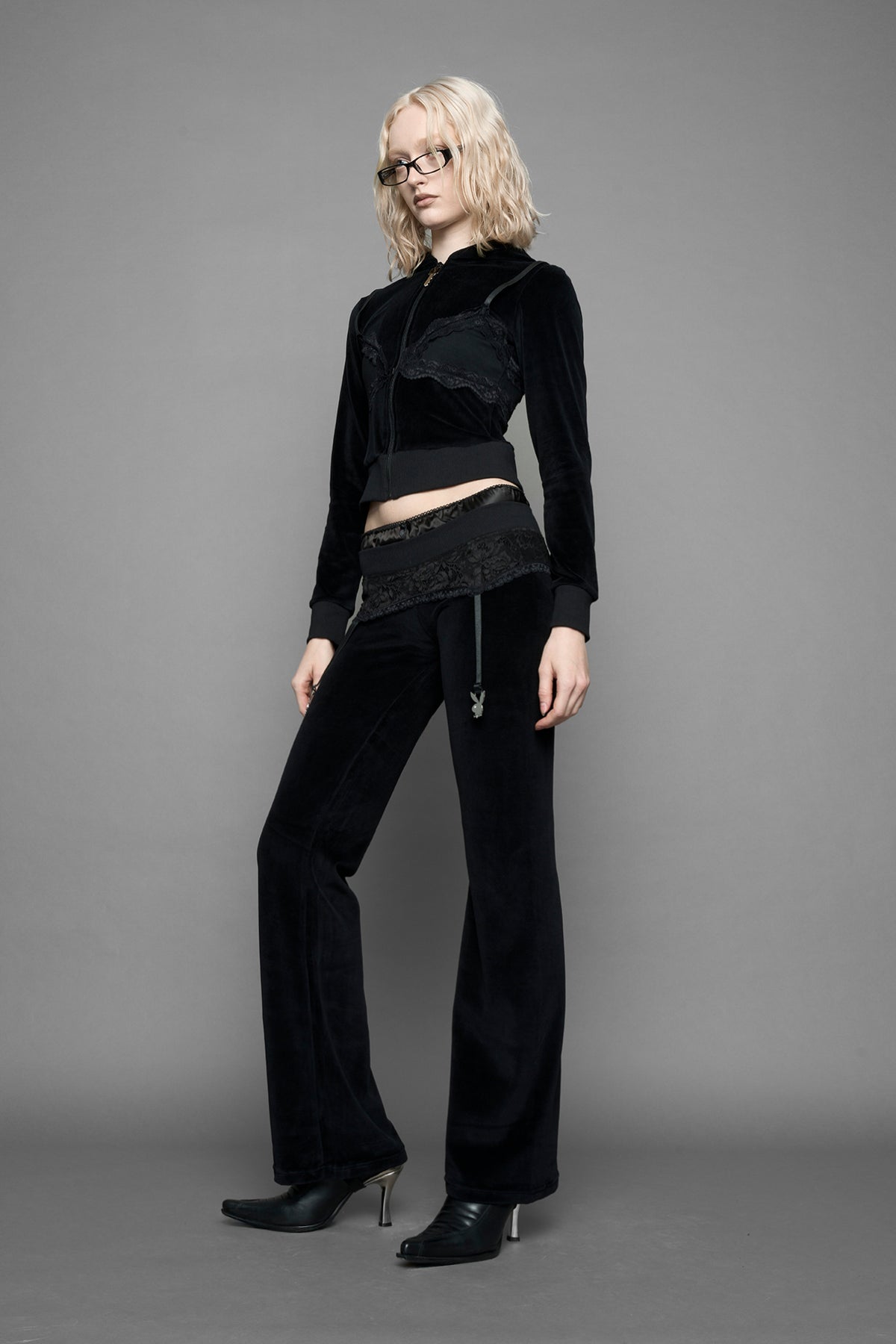 A female model wearing black velvet tracksuit pants with a lingerie black lace garter and suspenders with metal silver Bunnys 