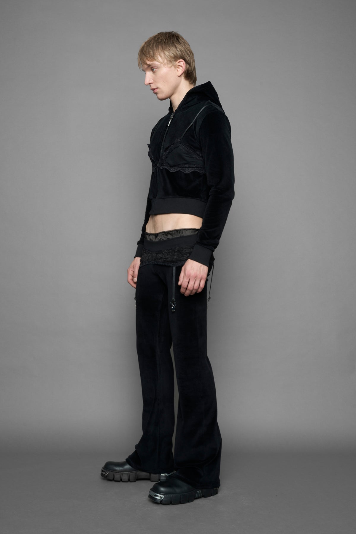 A female model wearing black velvet tracksuit pants with a lingerie black lace garter and suspenders with metal silver Bunnys 
