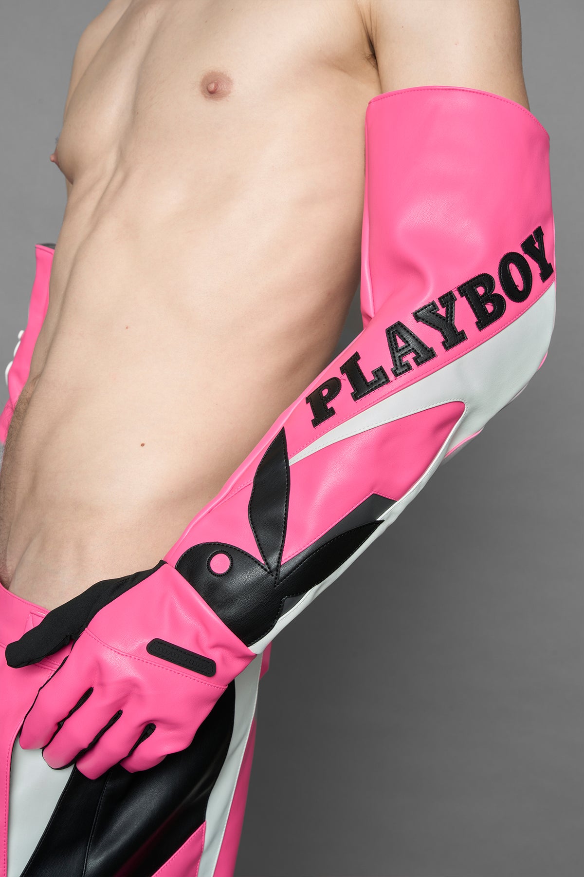 A model wears long motocross inspired pink vegan Leather gloves with white and grey style paneling and black PU Leather 'Namilia' and 'Playboy' embroidery and a 'Playboy x Namilia' Rubbertag.