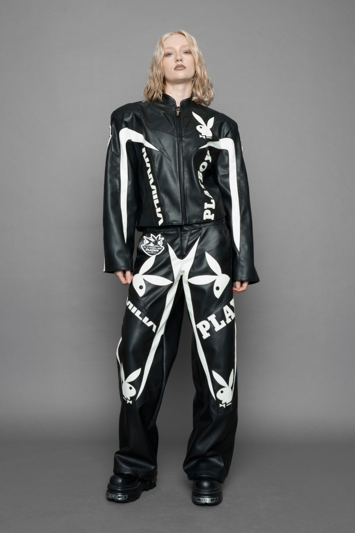 model wearing black vegan leather zip-up jacket with white PU leather 'Namilia' and 'Playboy' embroidery and black and white paneling. On the left chest there is a white Playboy Bunny Embroidery.