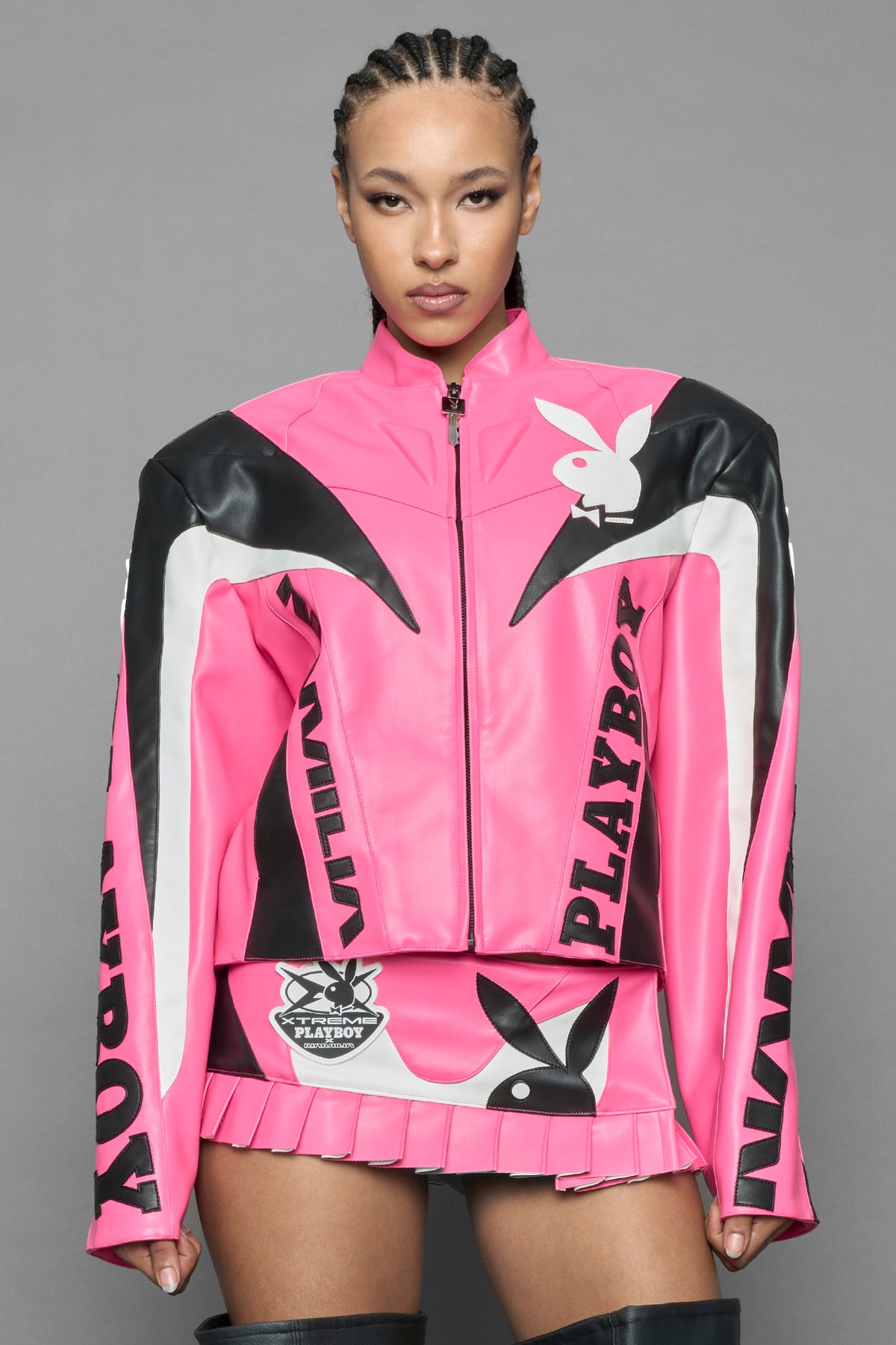 model wearing pink vegan leather zip-up jacket with black PU leather 'Namilia' and 'Playboy' embroidery and black and white paneling. On the left chest there is a white Playboy Bunny Embroidery.