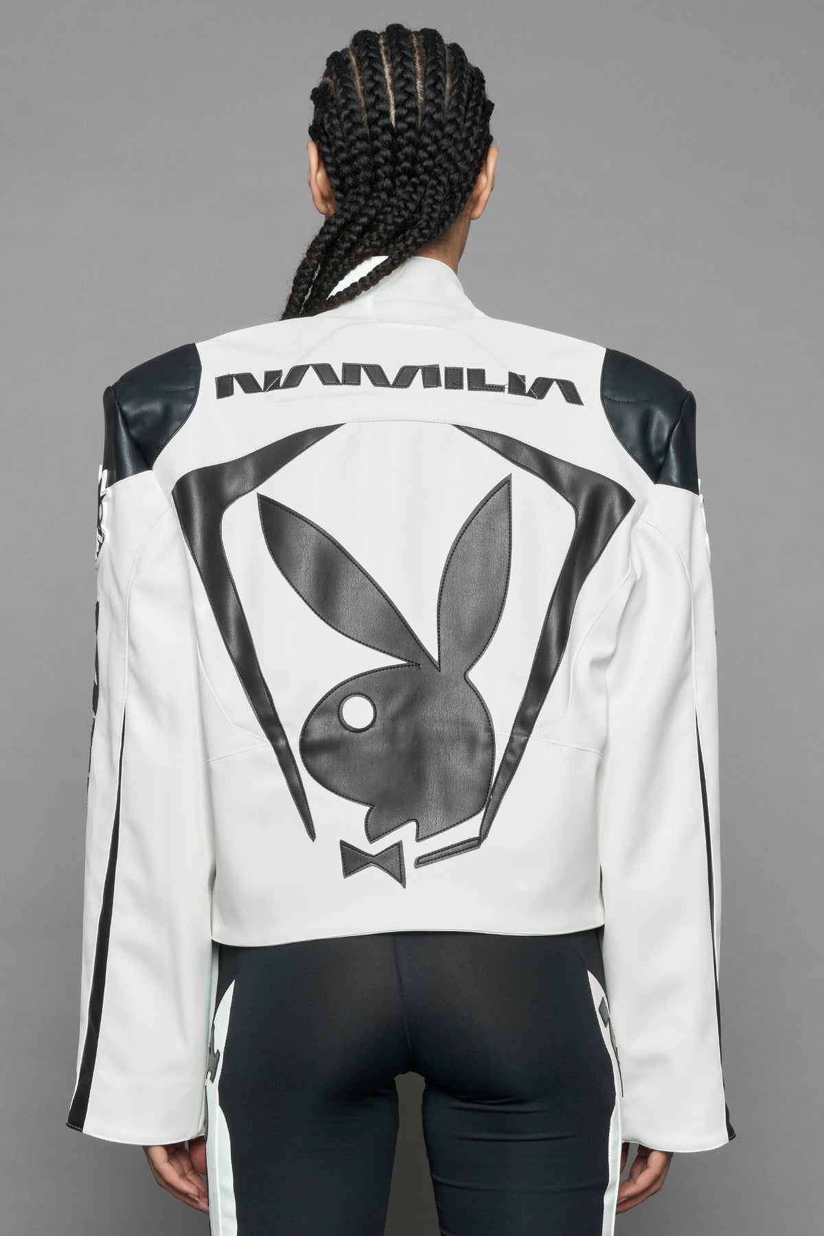model wearing white vegan leather zip-up jacket with black PU leather 'Namilia' and 'Playboy' embroidery and black and white paneling. On the left chest there is a white Playboy Bunny Embroidery.