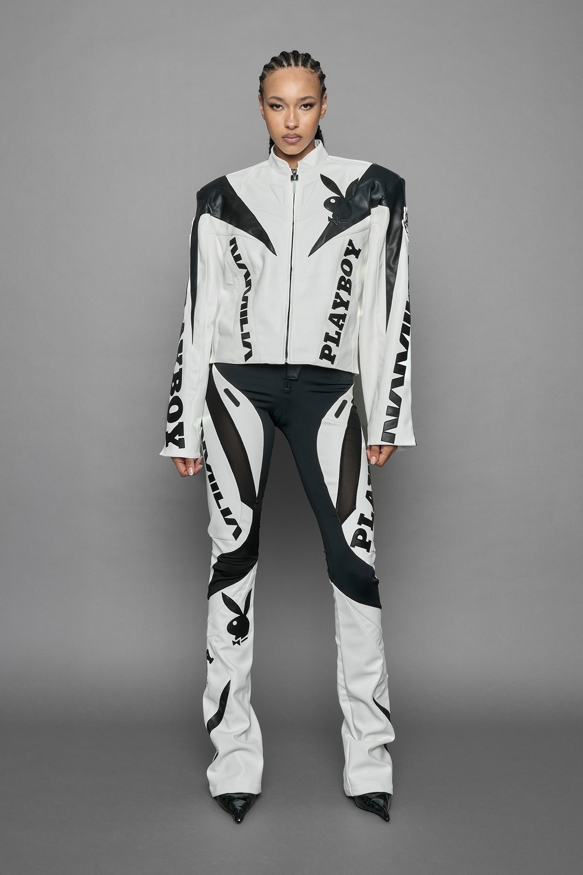 model wearing white vegan leather zip-up jacket with black PU leather 'Namilia' and 'Playboy' embroidery and black and white paneling. On the left chest there is a white Playboy Bunny Embroidery.