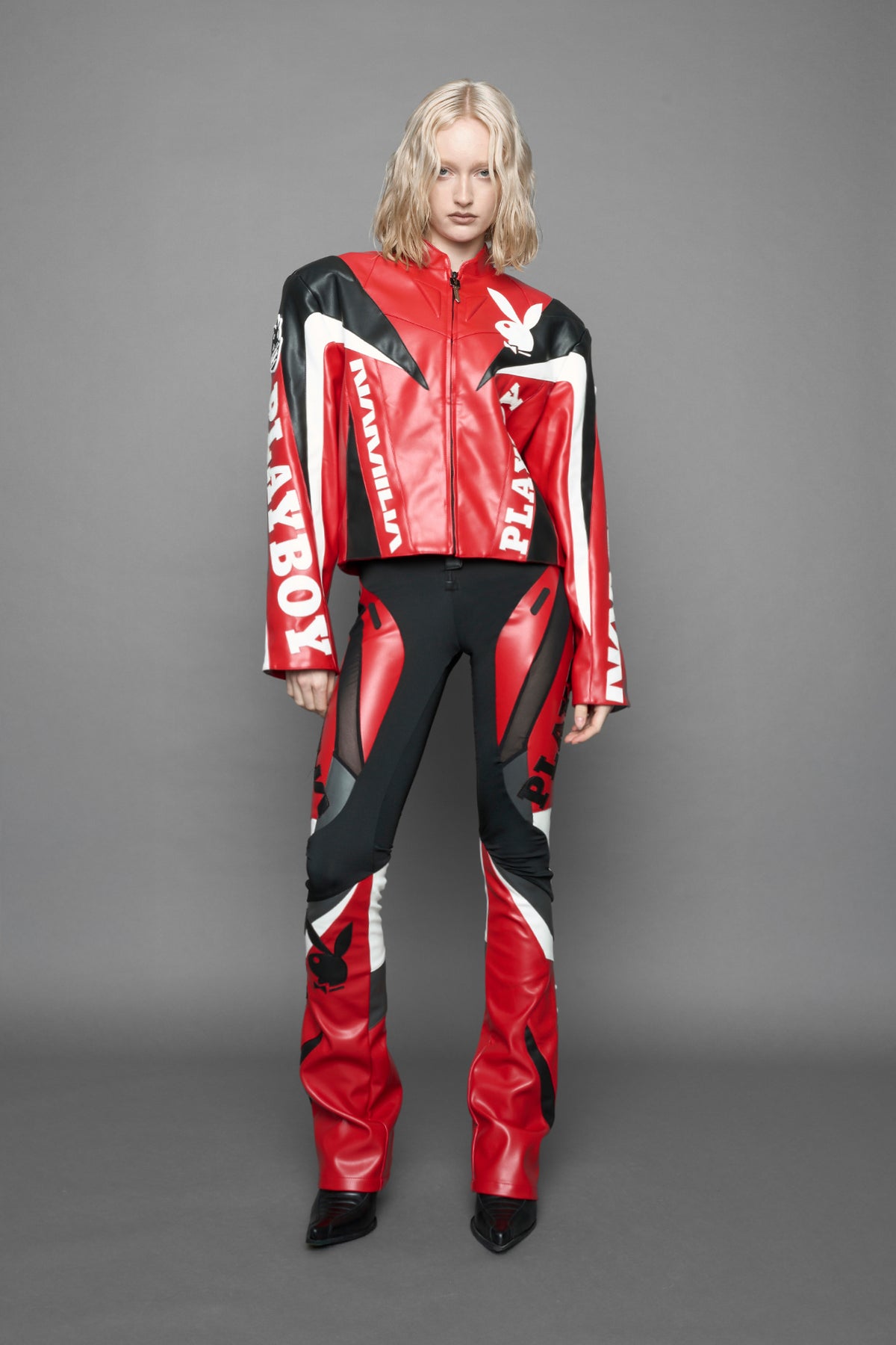 model wearing red vegan leather zip-up jacket with black PU leather 'Namilia' and 'Playboy' embroidery and black and white paneling. On the left chest there is a white Playboy Bunny Embroidery.