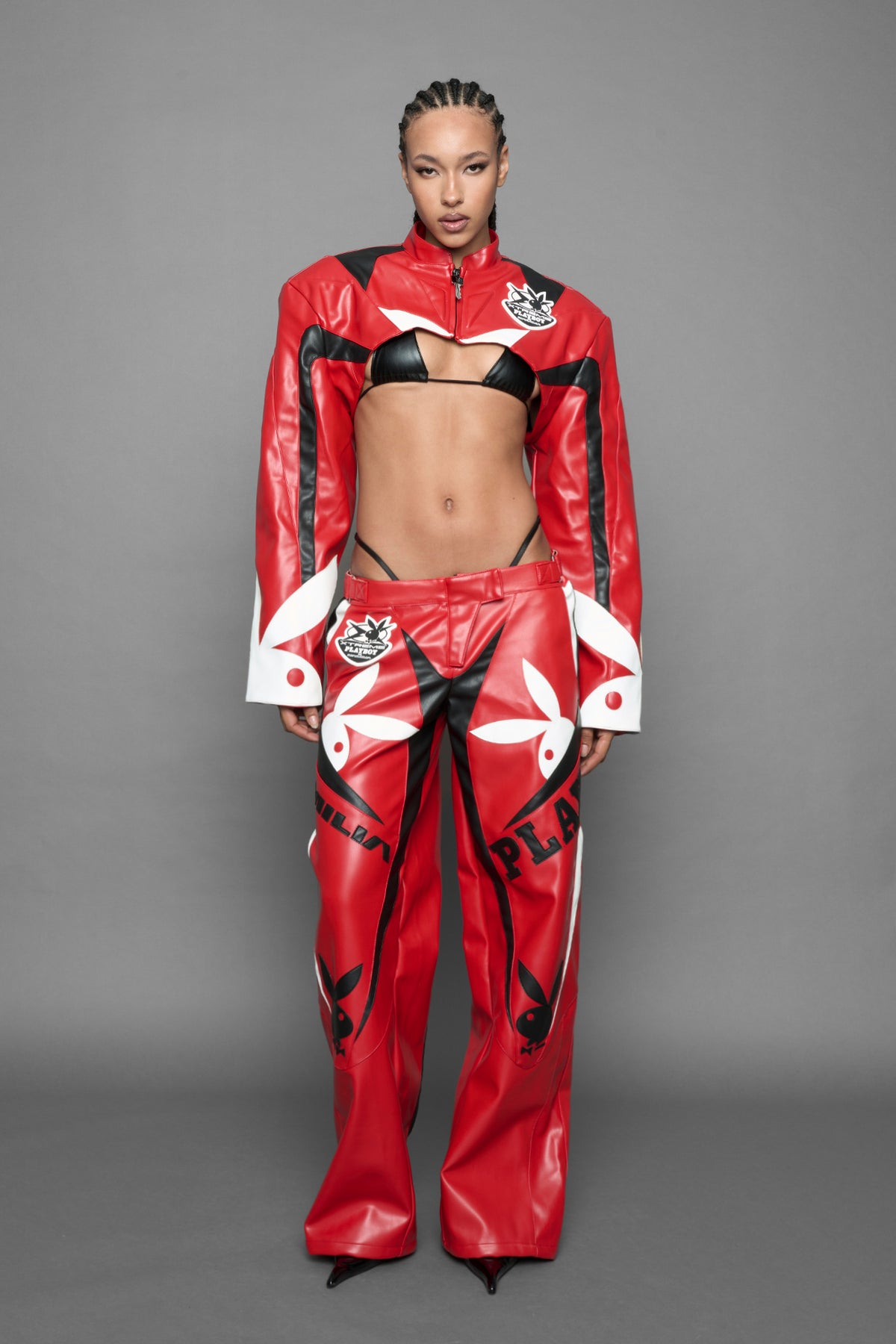 A female model is wearing red PU Leather pants with bold white Playboy bunny logos and white 'Namilia' Embroidery and rubber tag.