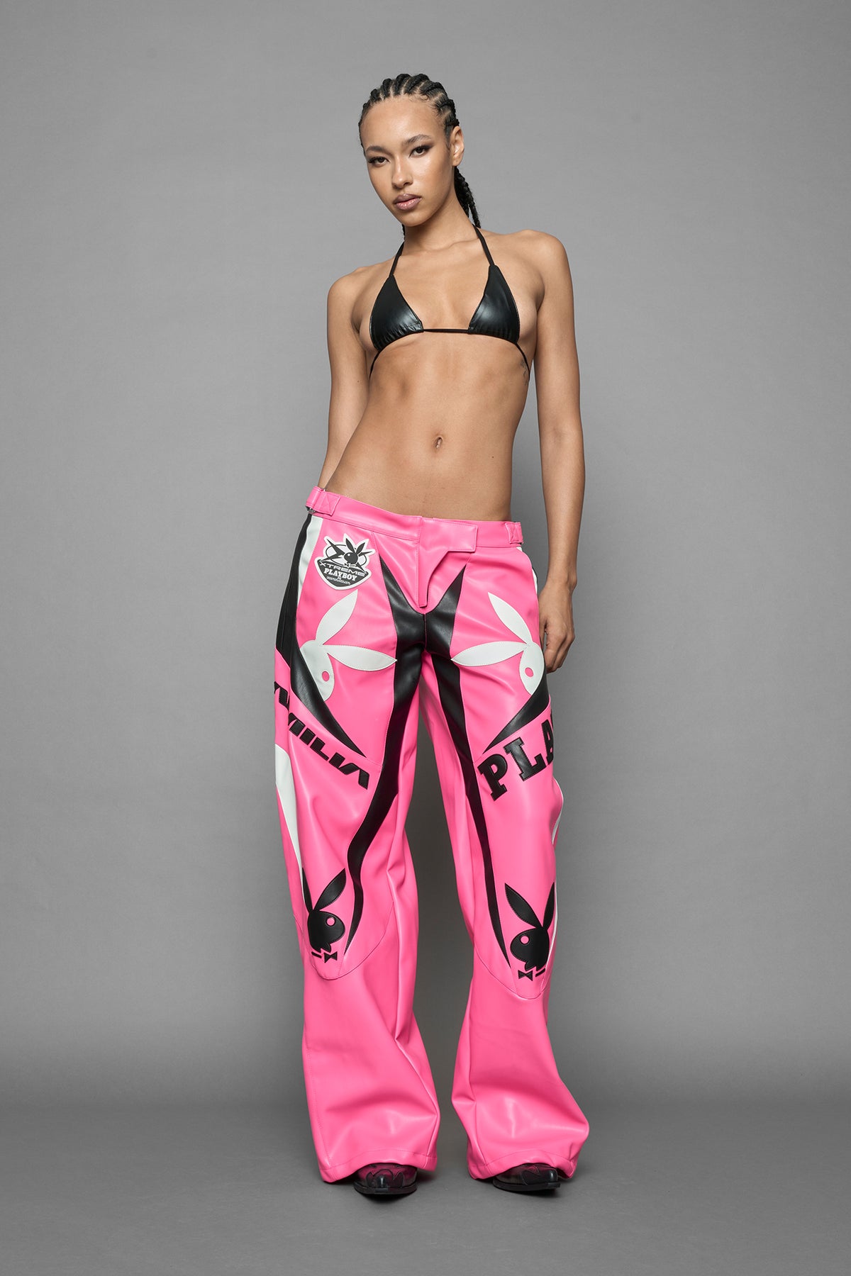 A female model is wearing pink PU Leather pants with bold white Playboy bunny logos and white 'Namilia' Embroidery and rubber tag.